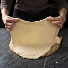 Ręce rozciągają elastyczne ciasto na pizzę, idealne do szybkiego przepisu na ciasto do pizzy.