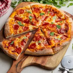 Pyszna pizza z pepperoni i świeżą bazylią, pokrojona na kawałki, leży na drewnianej desce. Obok sos pomidorowy i nóż do pizzy.