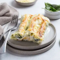 Pyszne cannelloni ze szpinakiem, zapieczone pod beszamelem i serem, na talerzu z widelcem i serwetką.