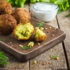 Chrupiące falafel na desce, jeden przekrojony, z sosem jogurtowym i koperkiem. Idealny falafel przepis.