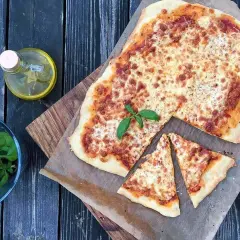 Pyszna pizza margherita z roztopionym serem i świeżą bazylią, obok buteleczka oliwy i miseczka z ziołami.