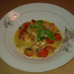 Krewetki z pomidorkami koktajlowymi w sosie winno maślanym, udekorowane bazylią.
