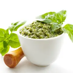 Aksamitne, zielone pesto w białej miseczce, ozdobione listkami bazylii. Obok drewniany tłuczek. To najlepsze pesto, jakie możesz sobie wyobrazić!