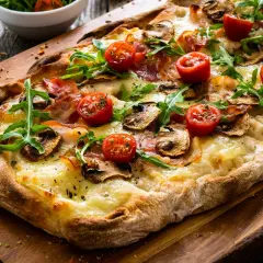 Pyszna pizza bez drożdży z pomidorkami, pieczarkami i rukolą na drewnianej desce.