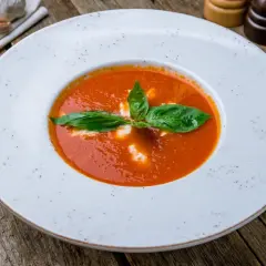 Aksamitny krem z pomidorów z listkami bazylii i śmietaną, podany na drewnianym stole.