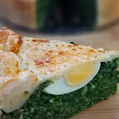 Kawałek torta pasqualina z zielonym nadzieniem i jajkiem, na drewnianej desce.