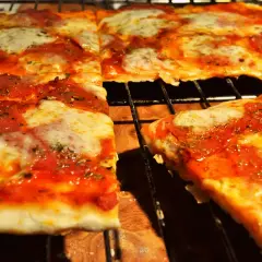 Pyszna pizza na cienkim cieście, z sosem pomidorowym i ciągnącym się serem, pokrojona na kwadraty.