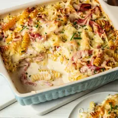 Pyszna zapiekanka makaronowa z serem i szynką, polana kremowym sosem, posypana szczypiorkiem.