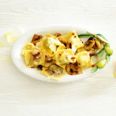 Pyszne ravioli z grzybami, posypane parmezanem i różowym pieprzem, podane na talerzu z gałązką oliwną.
