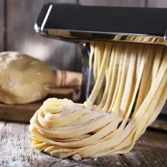 Świeży makaron wychodzi z maszynki, obok kulka ciasta. Idealny przepis na makaron domowy.