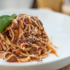 Pyszne spaghetti z sosem ragu, posypane parmezanem i udekorowane listkiem bazylii. Idealny przepis na obiad.