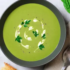 Aksamitna zupa szpinakowa ozdobiona śmietaną i natką pietruszki, podana z chrupiącym pieczywem.
