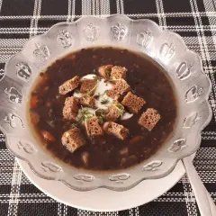 Gęsta, aromatyczna zupa z czarnej soczewicy, udekorowana grzankami i kleksem śmietany. Idealna na chłodne dni.