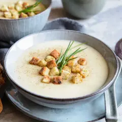 Aksamitna zupa czosnkowa z grzankami i szczypiorkiem, podana z chlebem i czosnkiem.