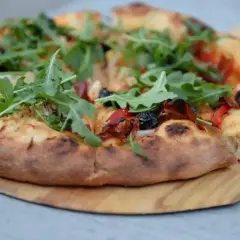 Pyszne ciasto na pizzę z rukolą, oliwkami i papryką, podane na drewnianej desce.
