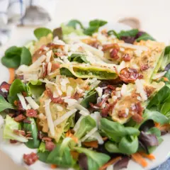Pyszne ravioli z kurczakiem, podane na sałatce z parmezanem i chrupiącym boczkiem.