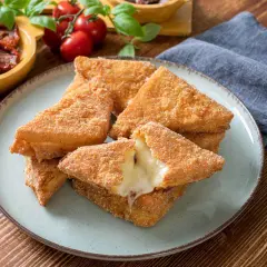 Chrupiące mozzarella in carrozza, z rozpływającym się serem w środku, na talerzu. Obok pomidorki i suszone pomidory.