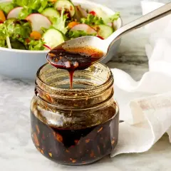 Łyżka polewa sałatkę gęstym, ciemnym sosem balsamicznym z słoiczka.