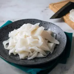 Na talerzu ułożone są białe, szerokie wstążki makaronu, przypominające capelli d'angelo. Obok leży nóż i deska do krojenia.