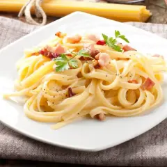 Pyszna carbonara włoska na białym talerzu, udekorowana natką pietruszki i posypana pieprzem.