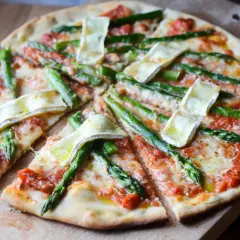 Pyszna pizza ze szparagami i serem brie, pokrojona na kawałki, prezentuje się apetycznie na drewnianej desce.