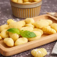Świeże, domowe gnocchi na drewnianej desce, gotowe do przygotowania według oryginalne gnocchi przepis. Obok czosnek i bazylia.