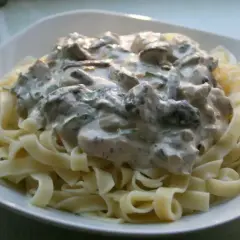 Pyszne tagliatelle z grzybami w kremowym sosie, podane na białym talerzu. Idealne danie dla miłośników grzybów.