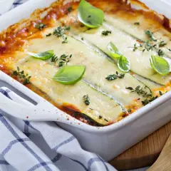 Pyszne lasagne z cukinią, zapieczone pod ciągnącym serem, ozdobione świeżą bazylią i tymiankiem.