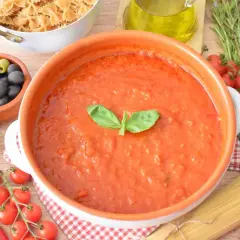 Aksamitny sos al pomodoro w glinianej misie, otoczony składnikami: makaronem, oliwkami, kaparami, pomidorkami, czosnkiem i bazylią.