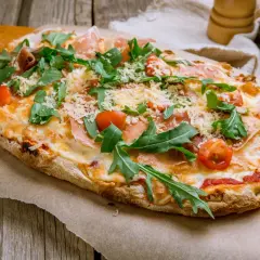 Pyszna pinsa romana z rukolą, pomidorkami i szynką parmeńską, posypana parmezanem, na drewnianym stole.