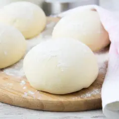 Kulki ciasta na desce, gotowe na idealne ciasto na pizzę. Lekko oprószone mąką, czekają na swoją kolej.