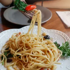 Widok z bliska na talerz pysznego spaghetti aglio e olio, z widelcem unoszącym porcję makaronu z bazylią i pomidorkiem.