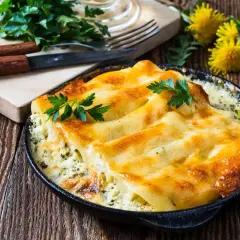 Zapiekane cannelloni w sosie, posypane serem i udekorowane natką pietruszki. Idealne danie na obiad.