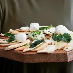 Carpaccio z selera z kulkami mozzarelli, jabłkiem i pastą ziołową na drewnianej desce.