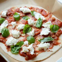 Pizza z sosem pomidorowym, świeżą bazylią i kawałkami puszystej mozzarella, gotowa do pieczenia.