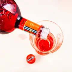 Nalewanie czerwonego Martini Fiero drinka do szklanki. Obok leży czerwona zakrętka z logo Martini.
