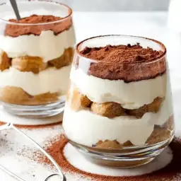 Dwa pucharki z deserem tiramisu. Warstwy biszkoptów, kremu i kakao. Idealny przepis na tiramisu.