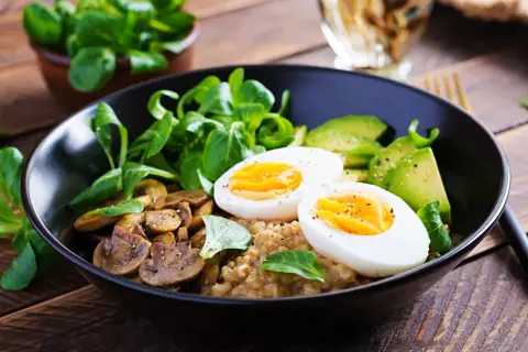 Pyszny bowl sniadaniowy z jajkiem na twardo, awokado, pieczarkami i świeżą sałatką na drewnianym stole.