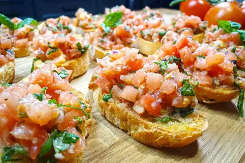 Pyszne bruschetta z pomidorami i bazylią, ułożone na drewnianej desce. Idealna przekąska na lato.