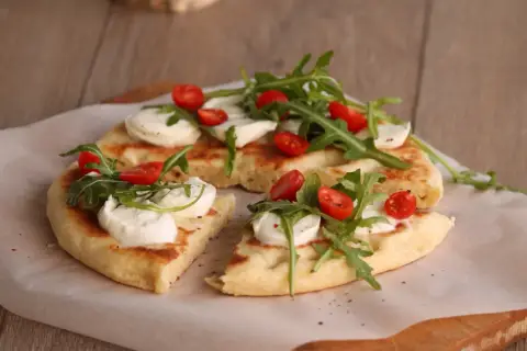 Pyszna focaccia z mozzarellą, pomidorkami koktajlowymi i rukolą, podana na papierze do pieczenia.
