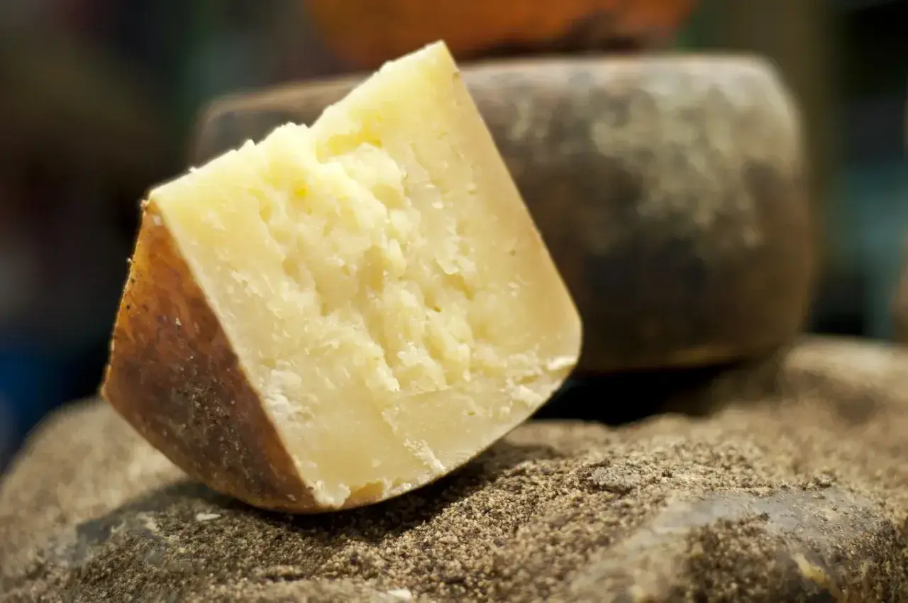 Kawałek twardego, żółtego sera, idealnego do pesto, leży na kamieniu obsypanym pieprzem.