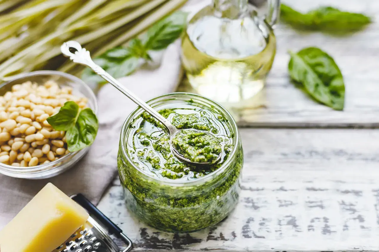 Pesto bazyliowe w słoiku, obok orzeszki piniowe, ser parmezan i oliwa. Idealne do makaronu, na grzanki i do sałatek.