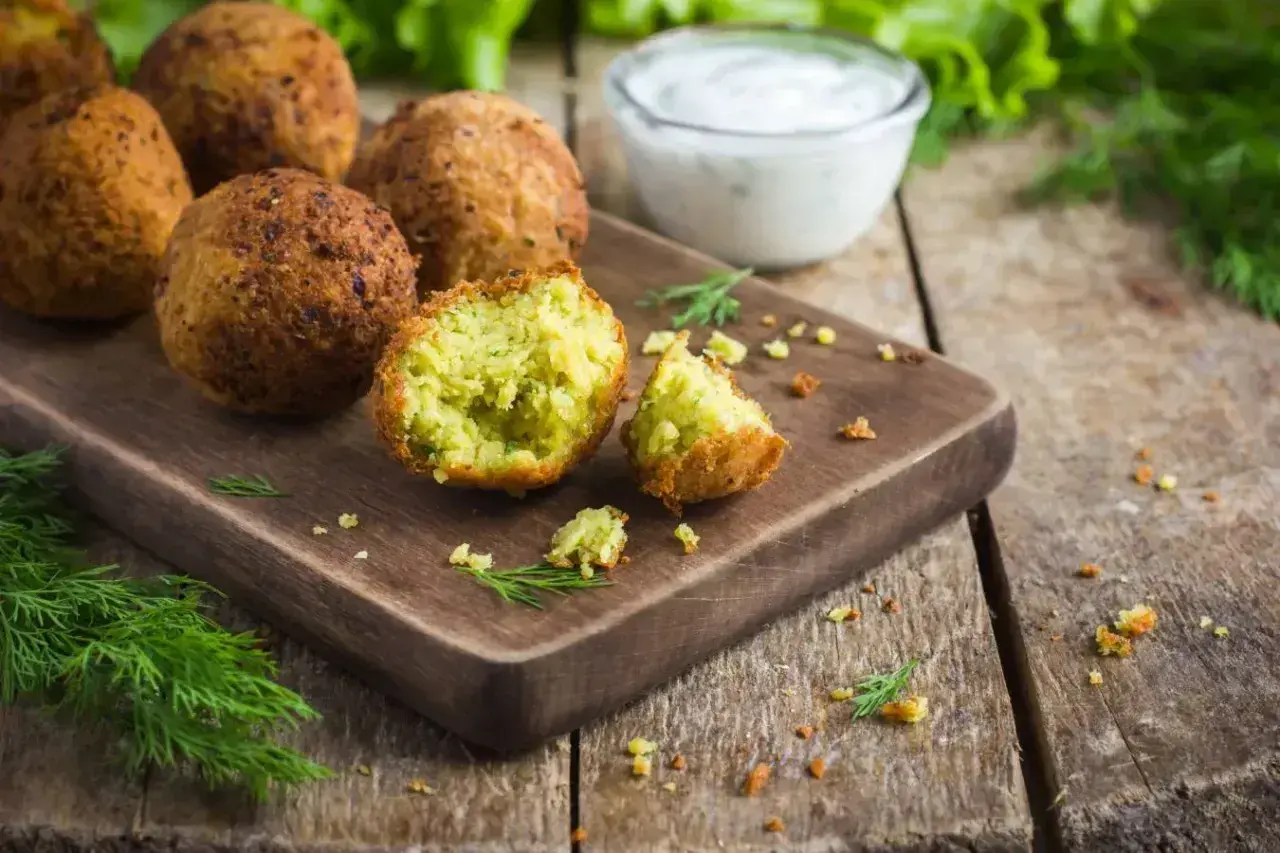 Chrupiące falafel na desce, jeden przekrojony, z sosem jogurtowym i koperkiem. Idealny falafel przepis.