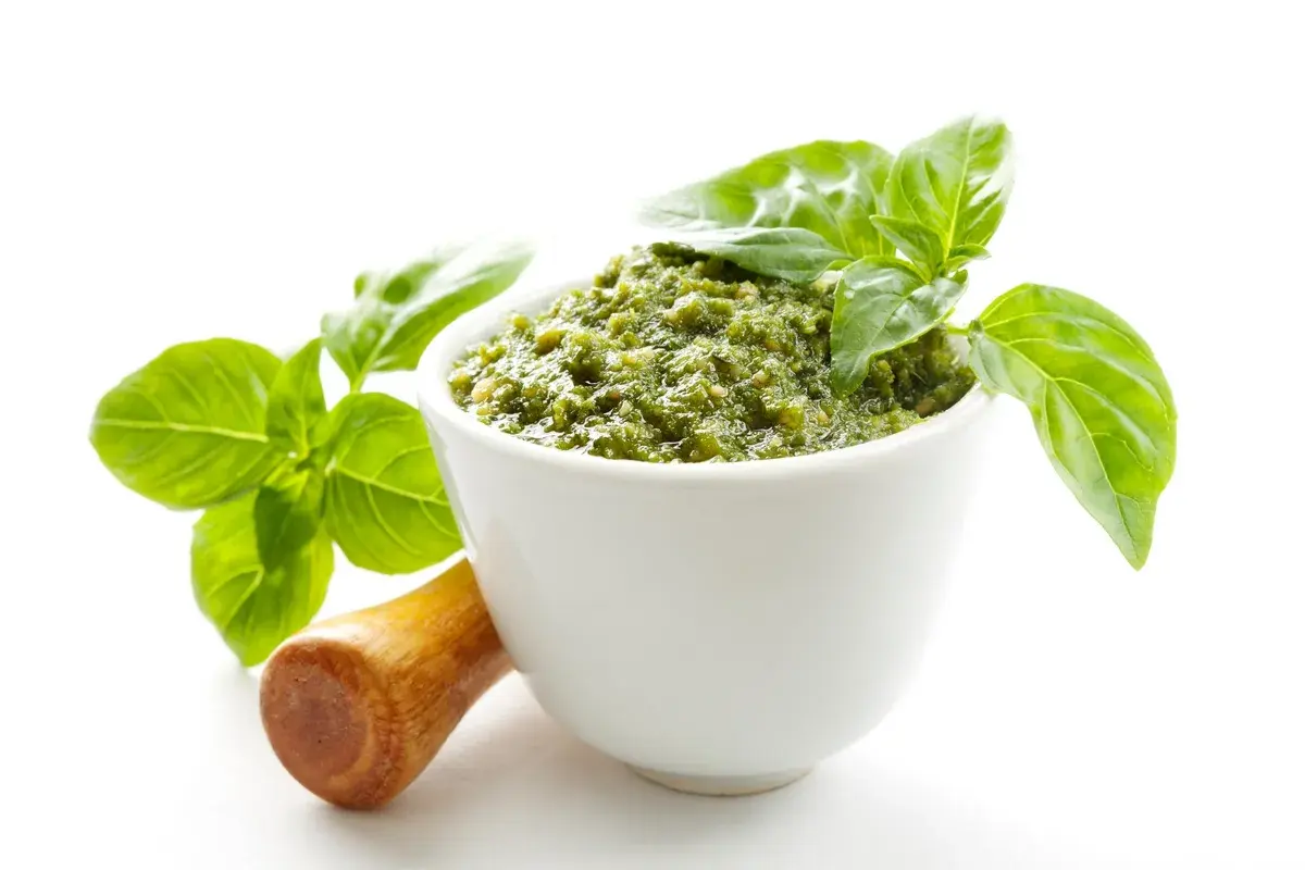 Aksamitne, zielone pesto w białej miseczce, ozdobione listkami bazylii. Obok drewniany tłuczek. To najlepsze pesto, jakie możesz sobie wyobrazić!