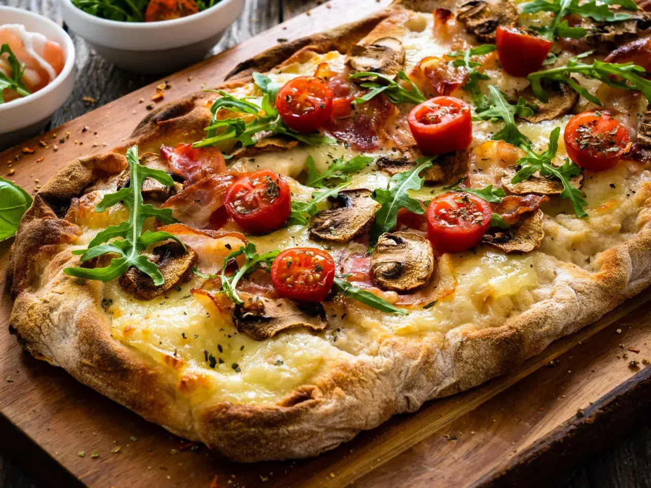 Pyszna pizza bez drożdży z pomidorkami, pieczarkami i rukolą na drewnianej desce.