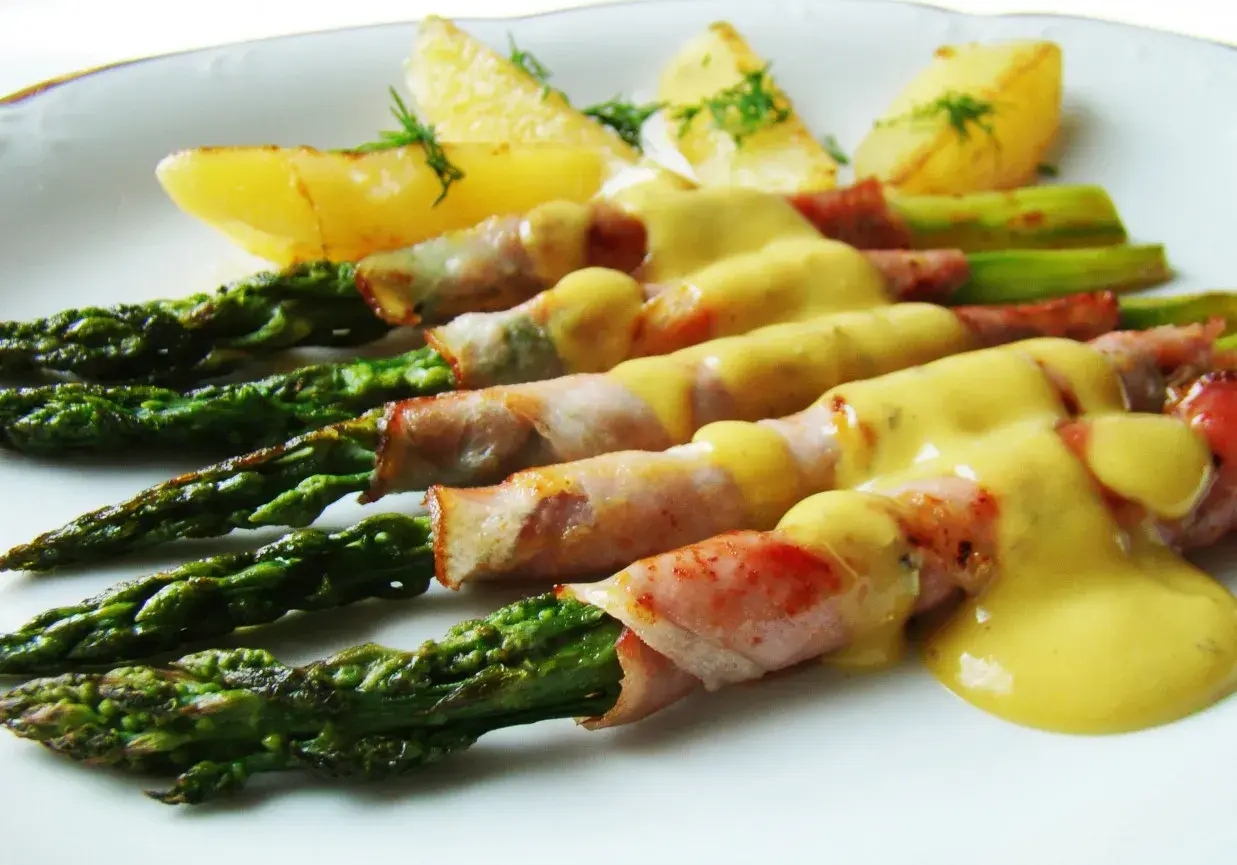 Zielone szparagi w szynce parmeńskiej, polane sosem, z pieczonymi ziemniakami. Pyszne danie.