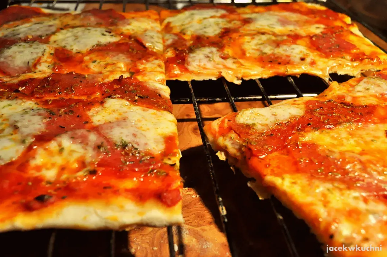 Pyszna pizza na cienkim cieście, z sosem pomidorowym i ciągnącym się serem, pokrojona na kwadraty.