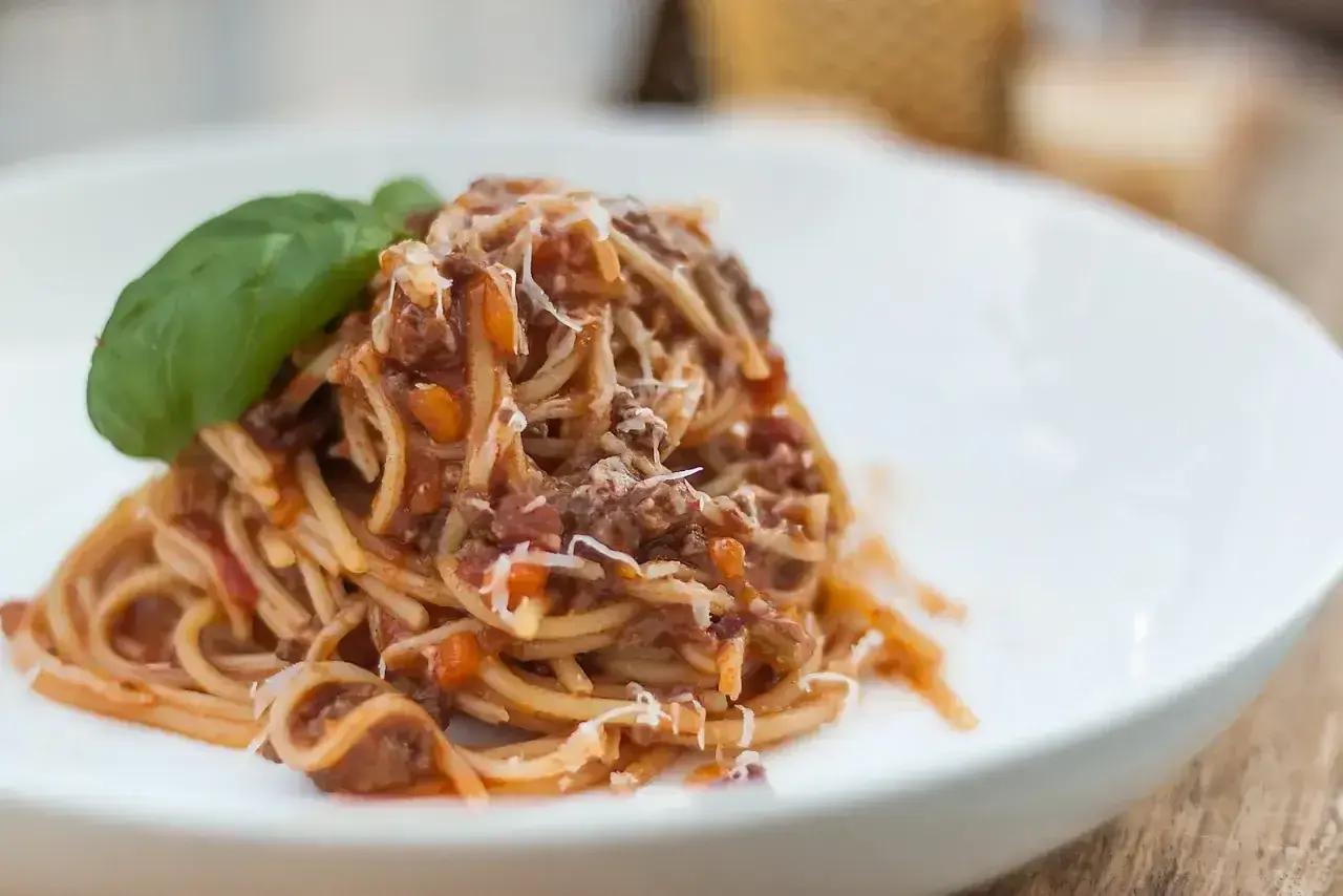 Pyszne spaghetti z sosem ragu, posypane parmezanem i udekorowane listkiem bazylii. Idealny przepis na obiad.