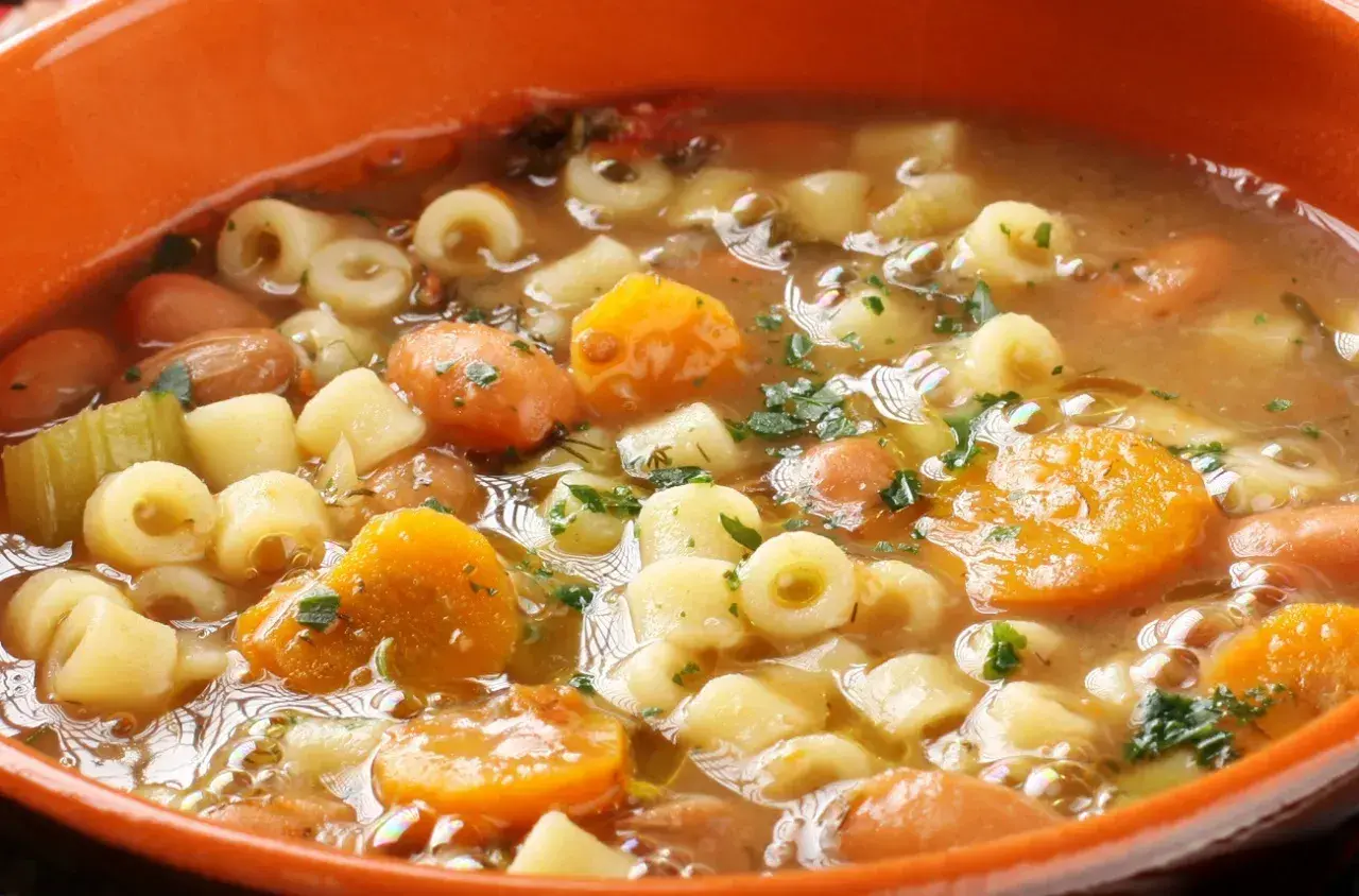 Gęsta, aromatyczna zupa minestrone z makaronem, fasolą, marchewką i ziemniakami, posypana natką pietruszki.