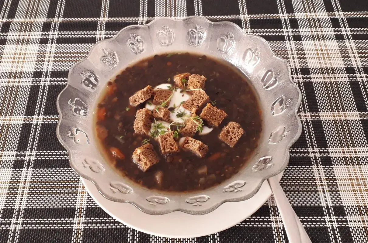 Gęsta, aromatyczna zupa z czarnej soczewicy, udekorowana grzankami i kleksem śmietany. Idealna na chłodne dni.